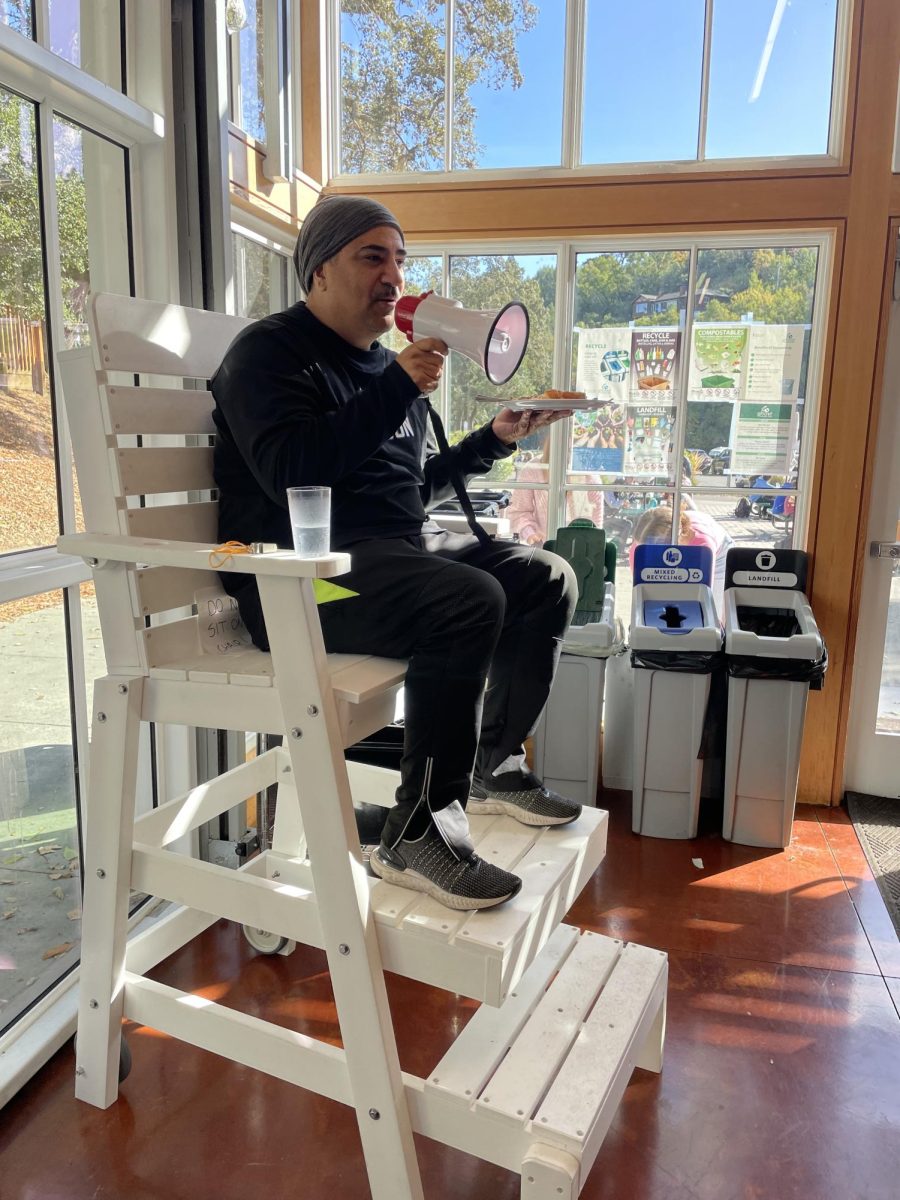 DEI Director JuanCarlos Arauz sits in the commons lifeguard chair and speaks into megaphone.